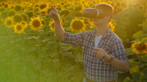 The-young-farmer-is-working-in-VR-glasses.-He-is-engaged-in-the-working-process.-It-is-a-beautiful-sunny-day-in-the-sunflower-field.